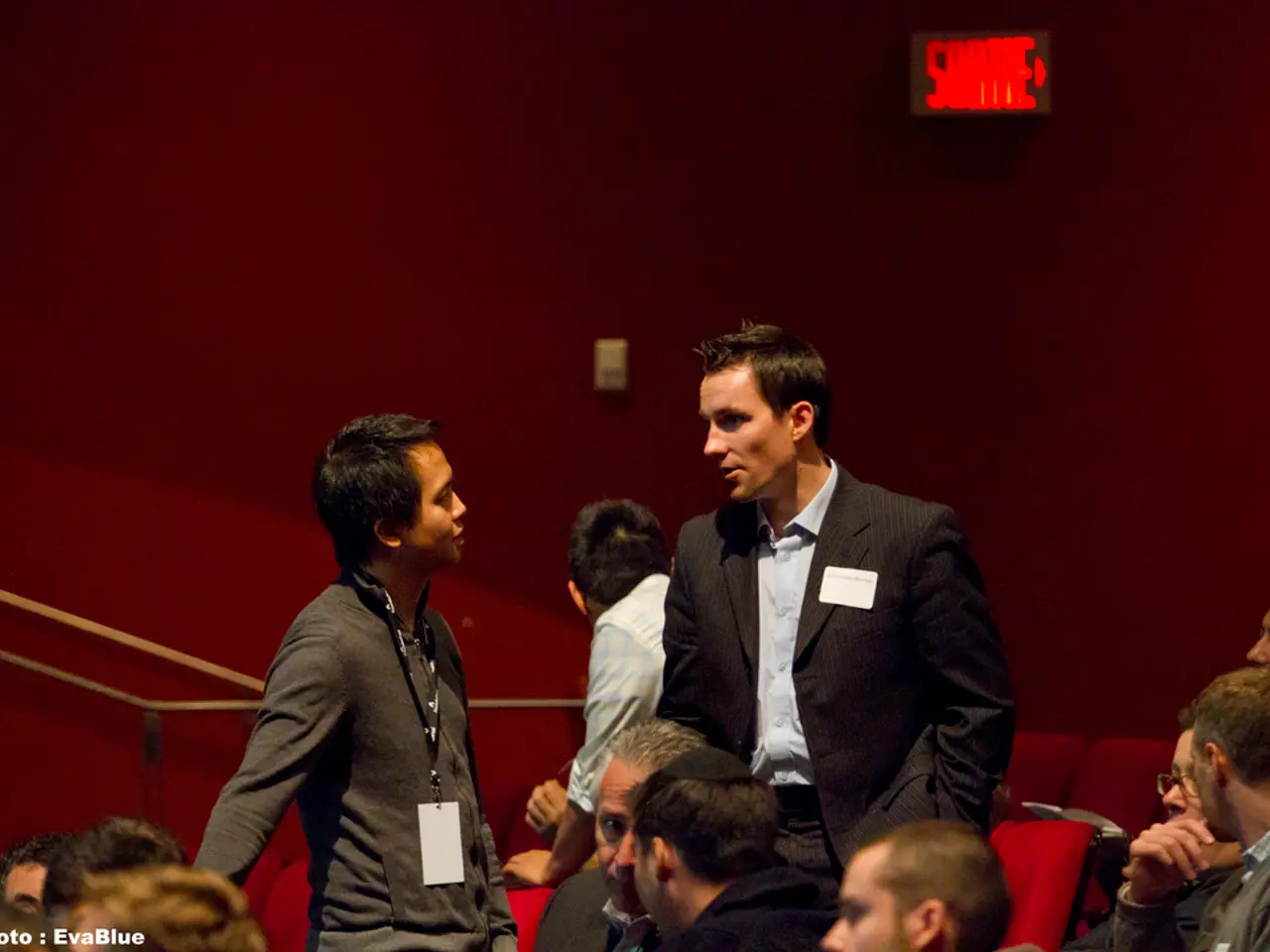 In this picture there are three people standing and there are group of people sitting on the...